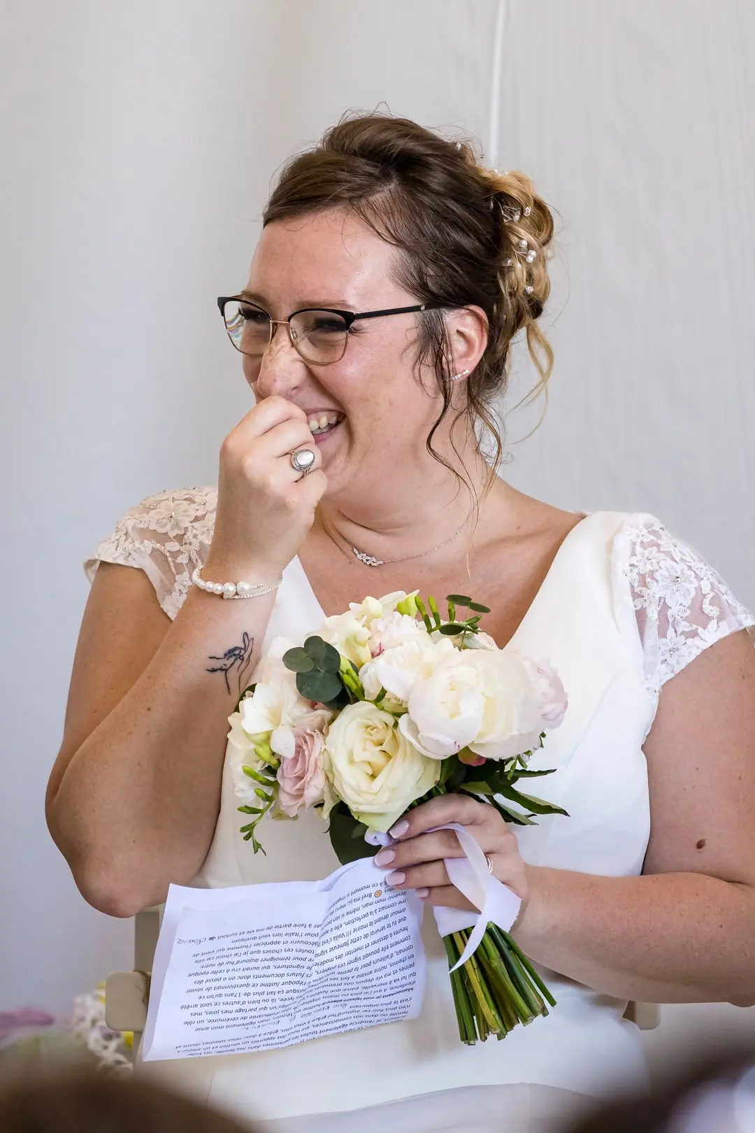 Mariée émue tenant un bouquet de fleurs et une lettre, photographiée lors de son mariage à Bourgoin-Jallieu par Laurent Pannetier.”